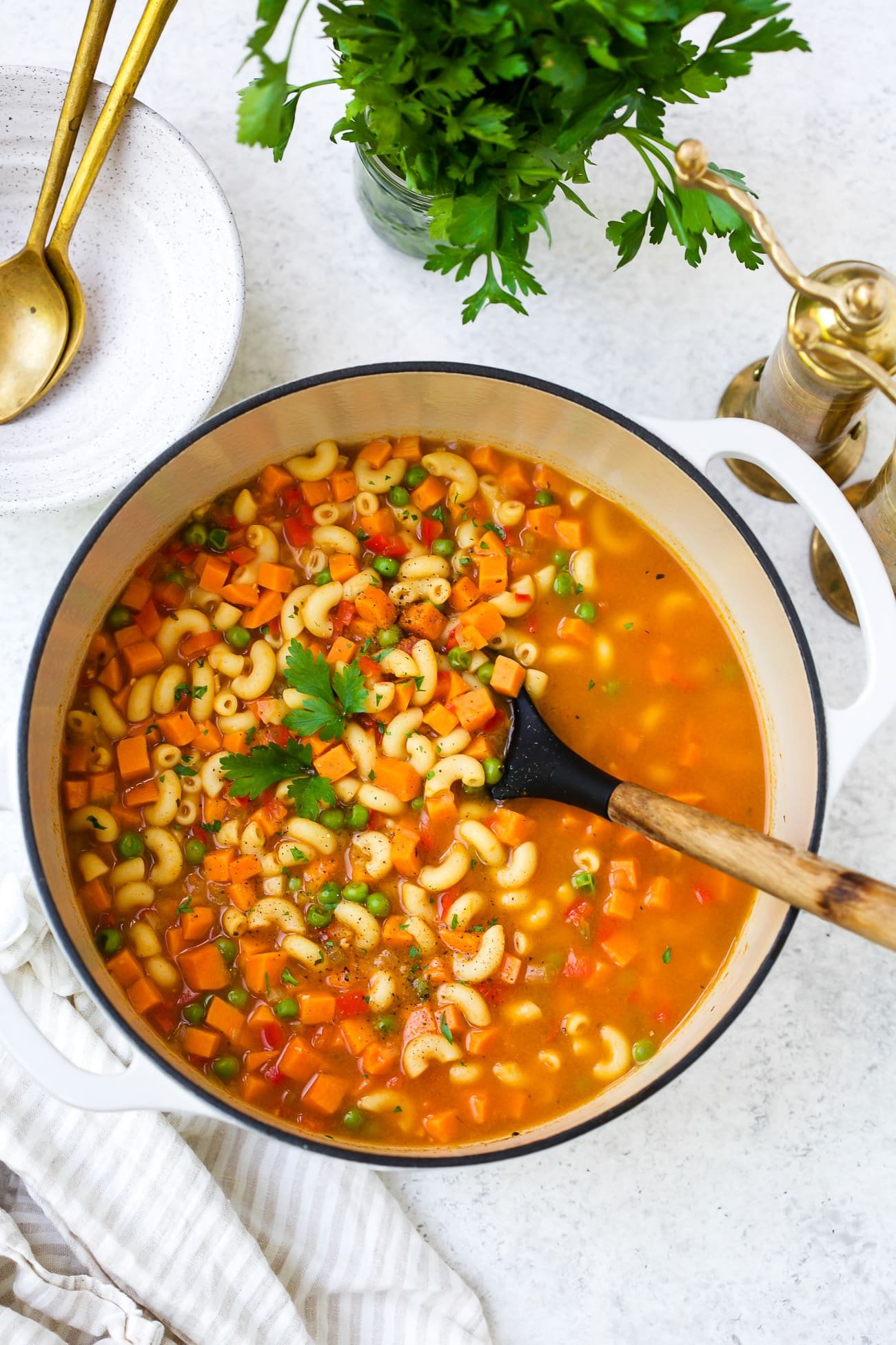 Closeup of a white pot of pasta soup with sweet potato and peas.