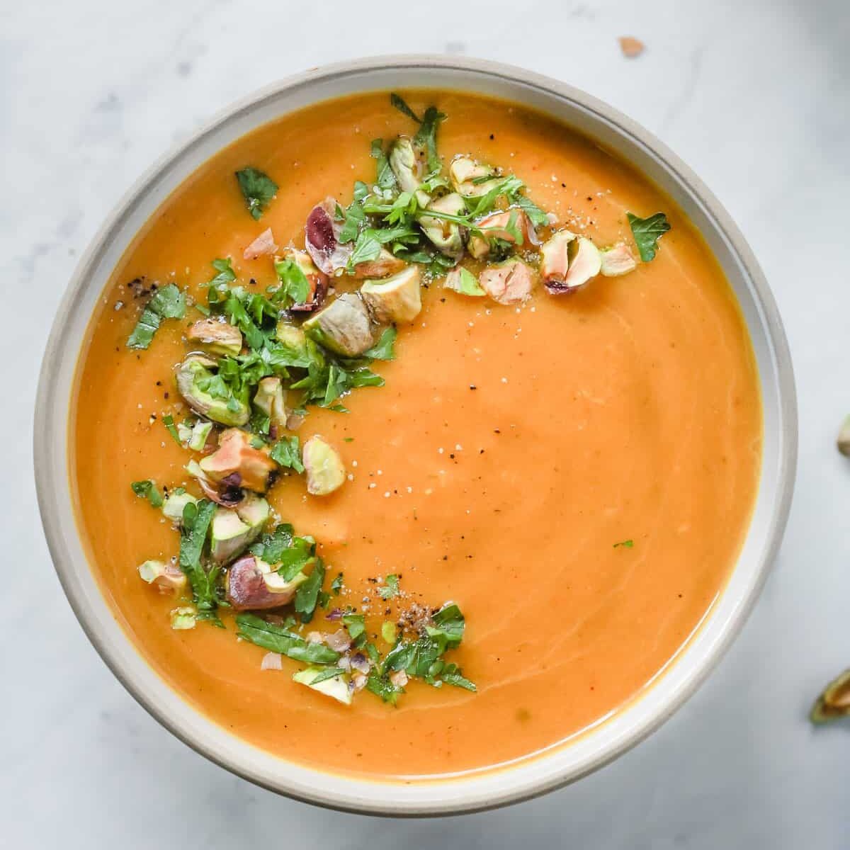 Overhead photo of a white bowl with butternut squash soup with garnish. 