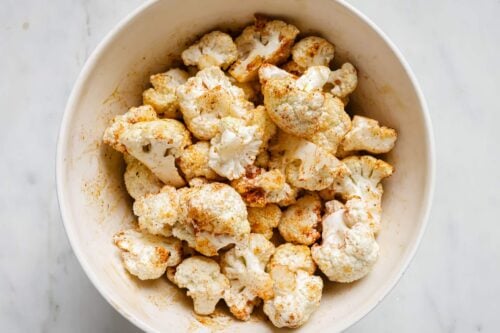 Seasoned raw cauliflower florets in a bowl.