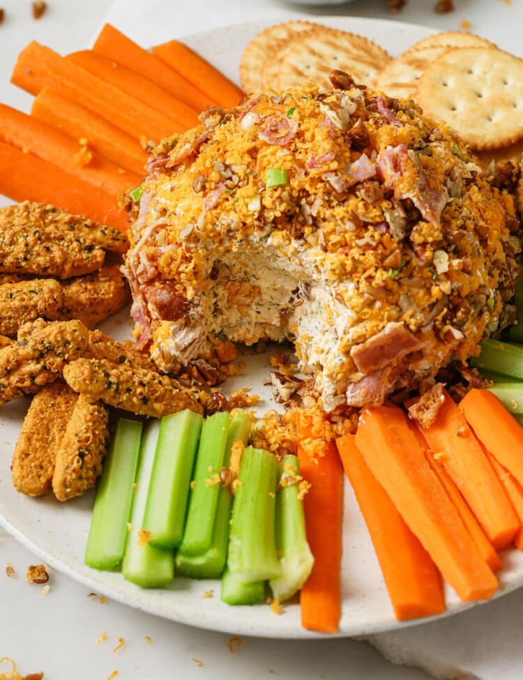 Cheese Ball on a plate with vegetables, crackers, and bread sticks.