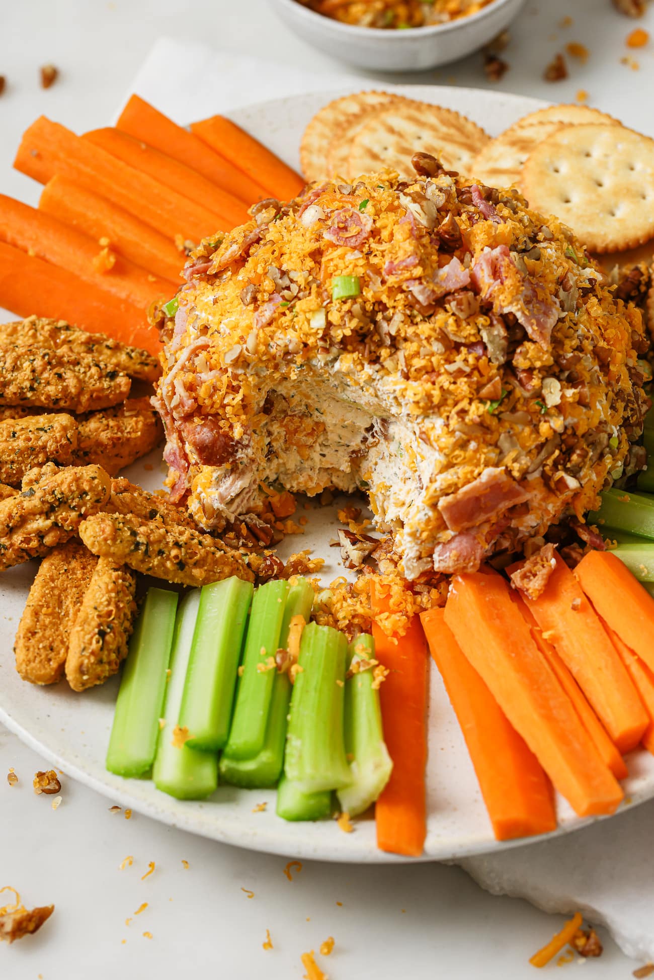 Cheese Ball on a plate with vegetables, crackers, and bread sticks. 