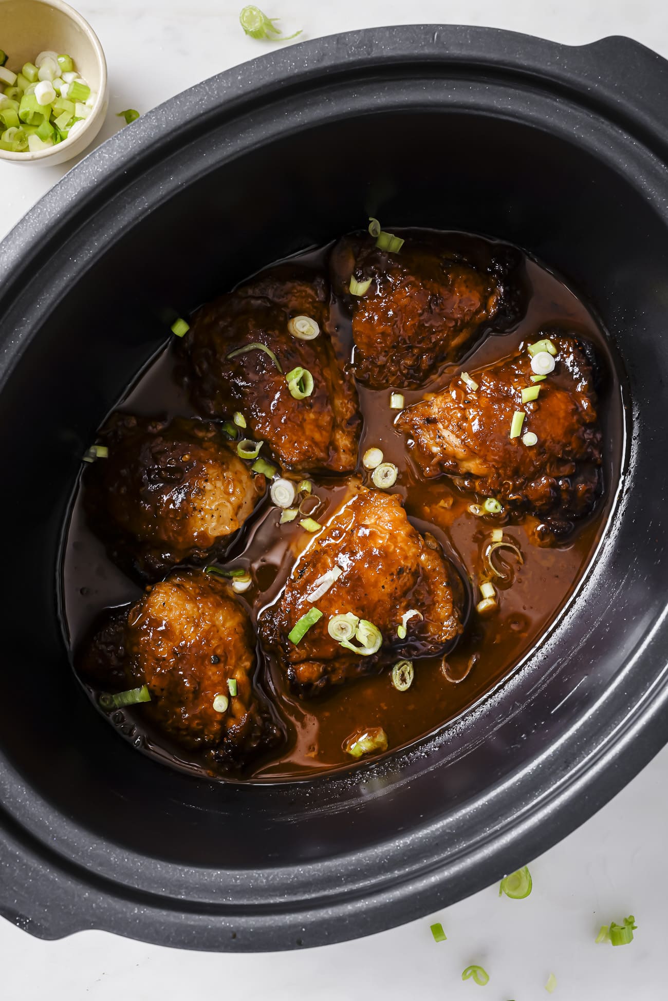 Chicken thighs in the slow cooker with sliced green onions.
