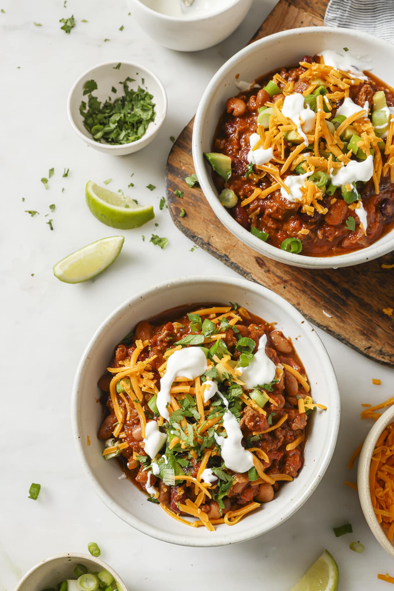 Two bowls of slow cooker chili with toppings.
