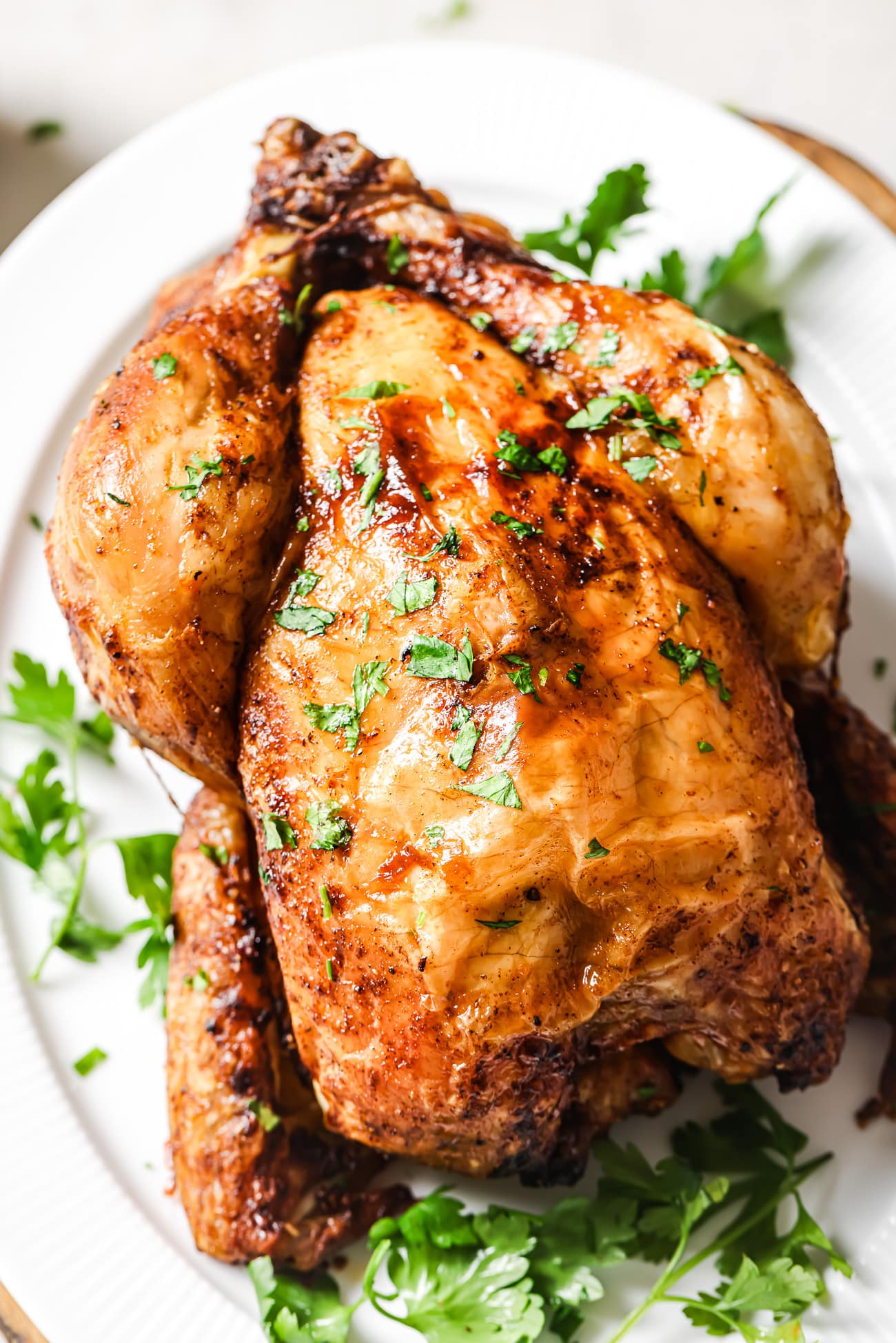 Air Fryer Whole Chicken on a while platter with chopped parsley on top. 