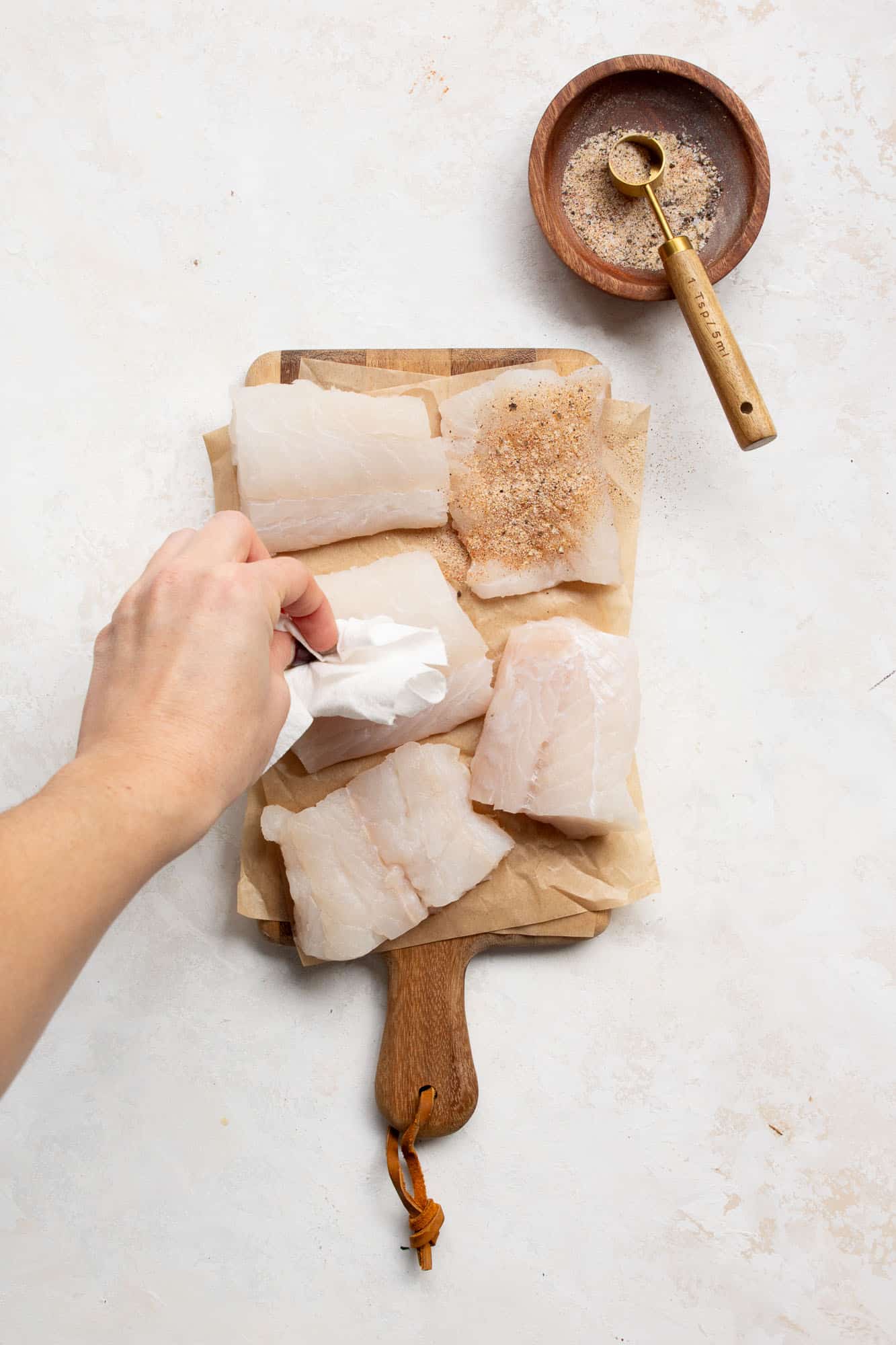 A hand patting the cod fish dry with a paper towel. 