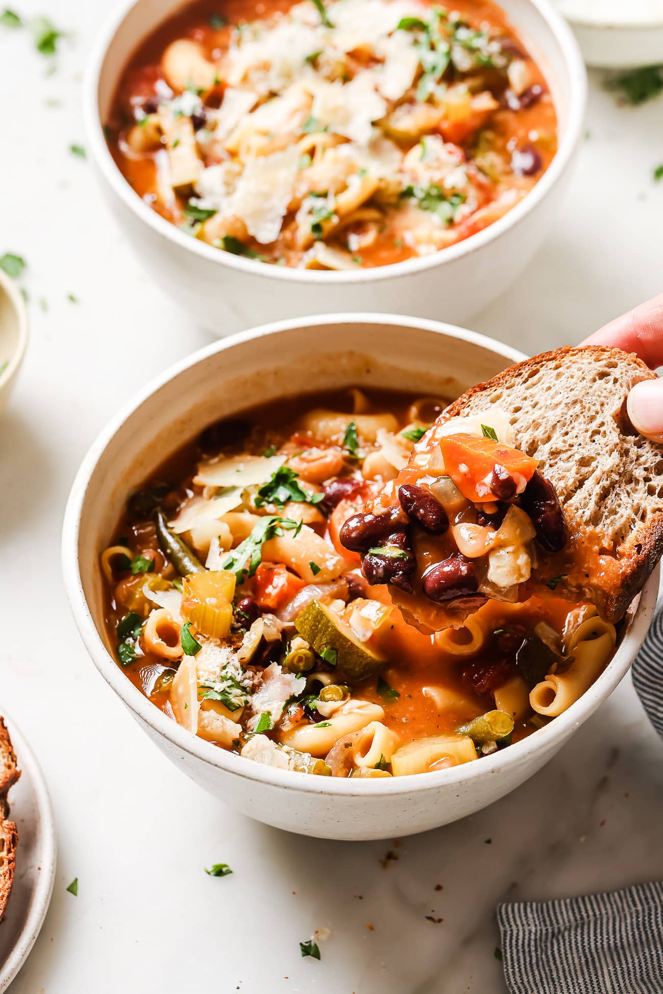A bowl of Minestrone Soup with a slice of fresh bread dipped into it. 