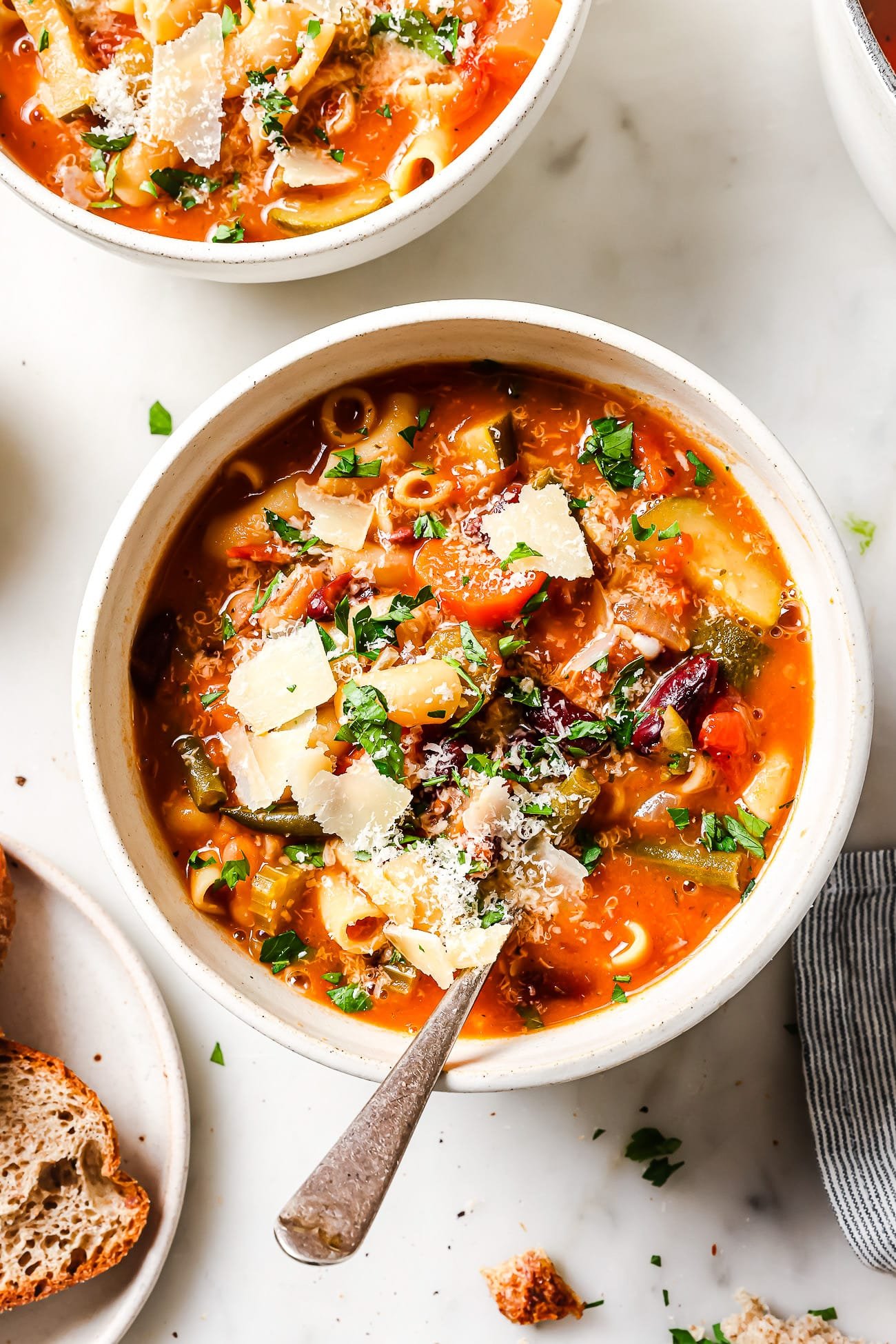 A bowl of Minestrone Soup garnished with fresh parsley and parmesan cheese.