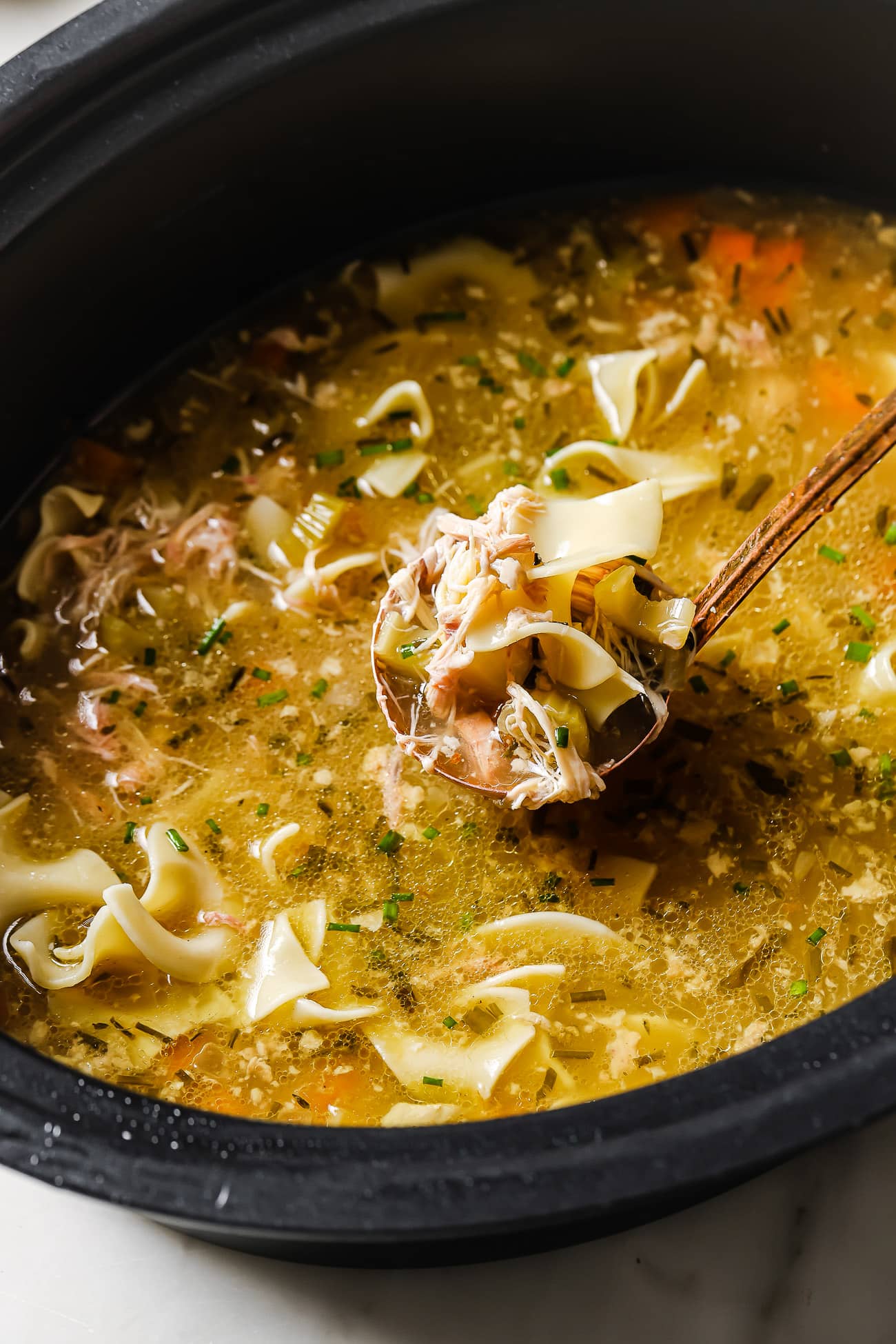 A closeup of slow cooker chicken noodles with a ladle of soup. 