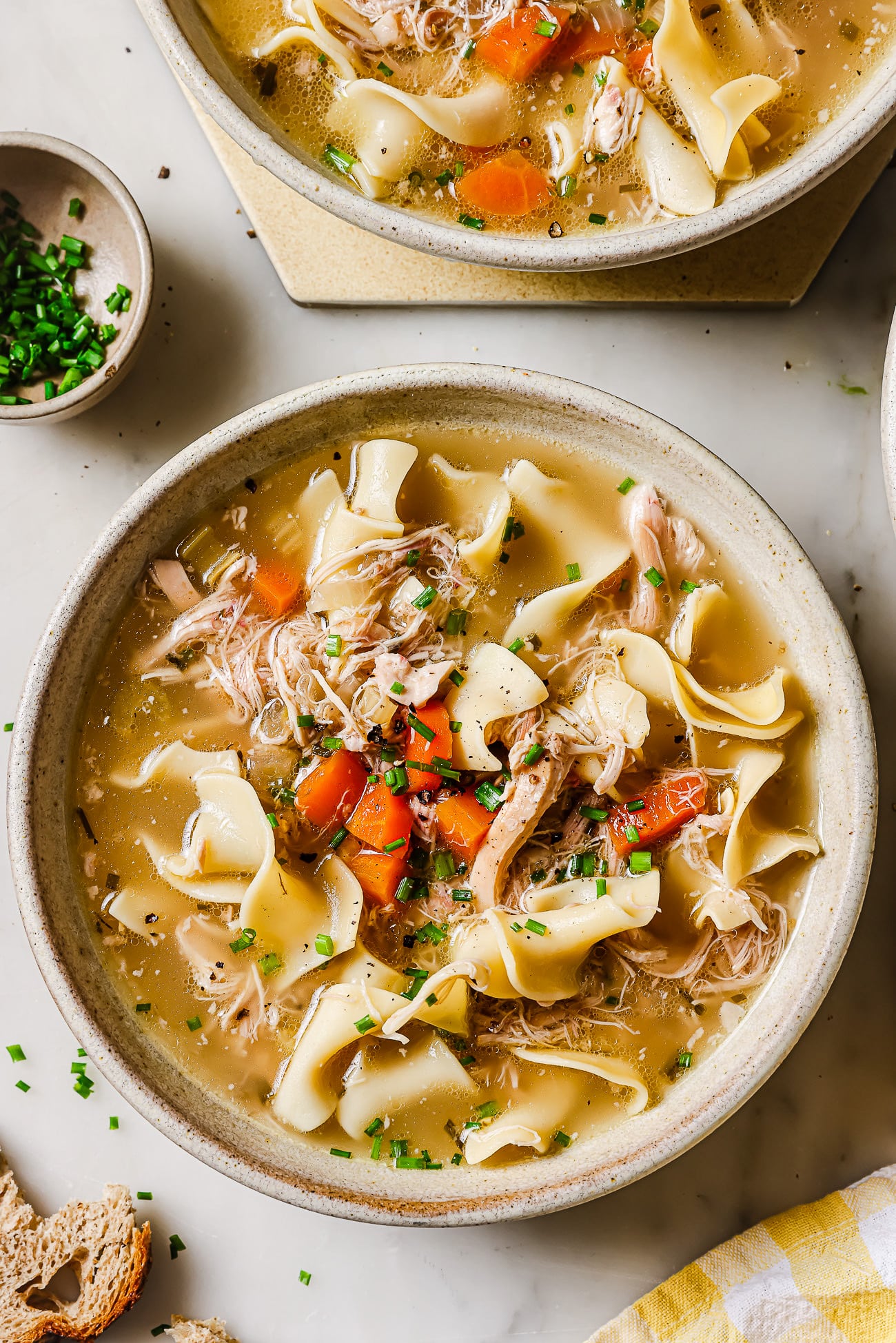 A bowl of slow cooker chicken noodles garnished with chives. 