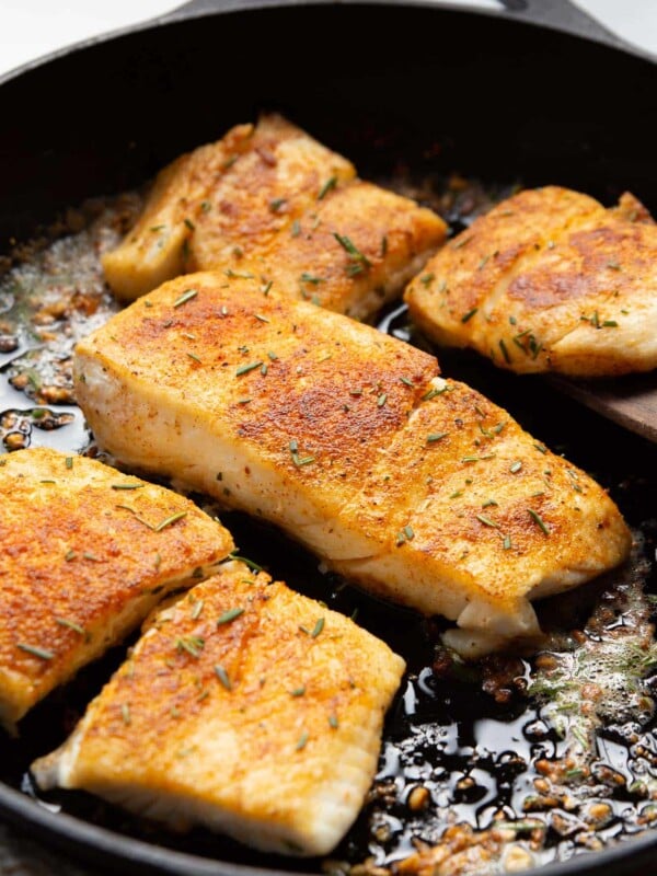 closeup of flaky garlic butter halibut fish in a cast iron skillet
