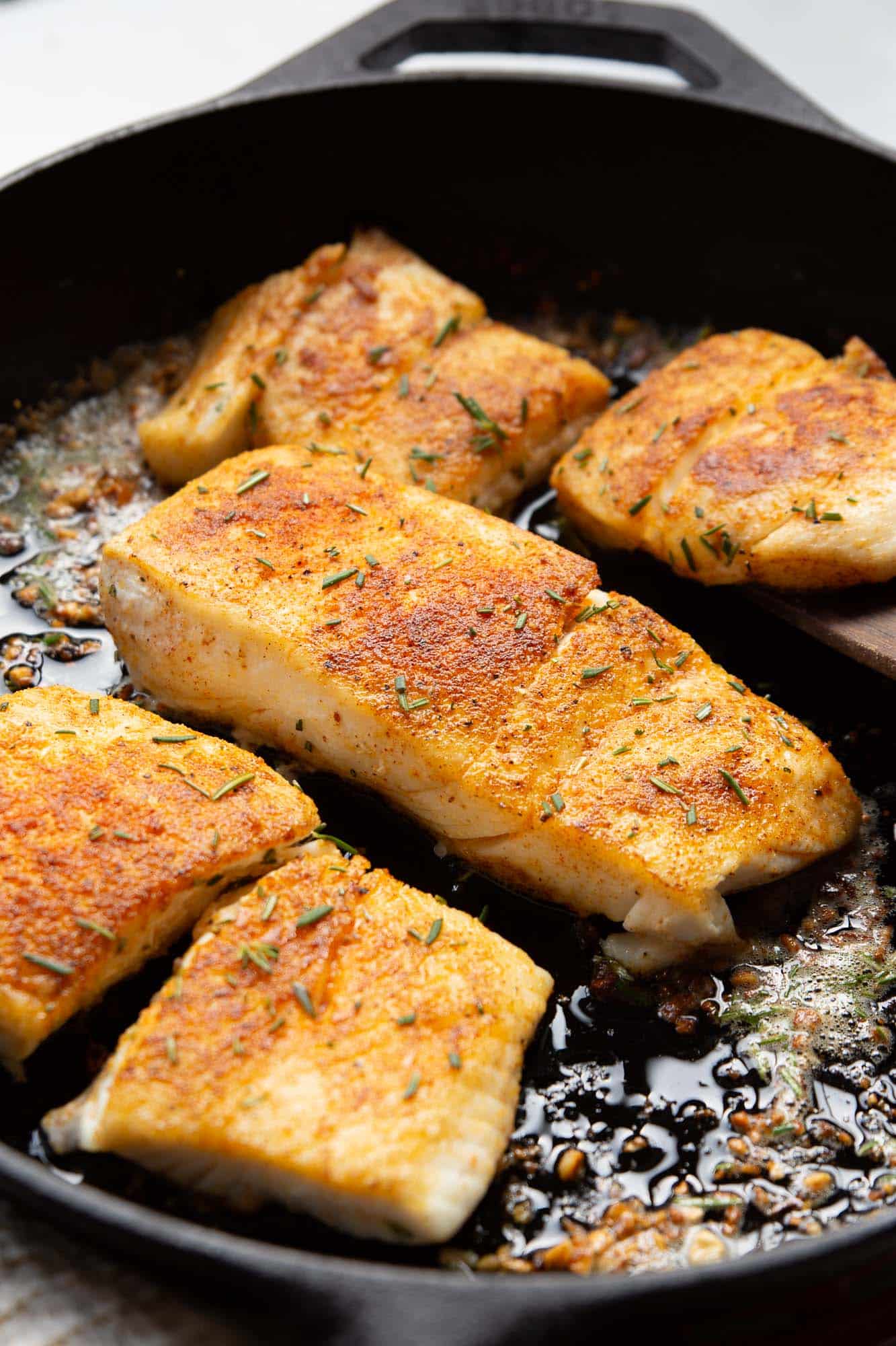 closeup of flaky garlic butter halibut fish in a cast iron skillet