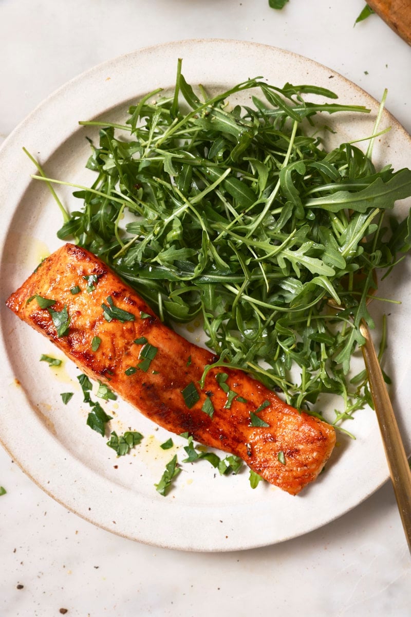 An air fryer trout fillet on a white plate with a salad. 