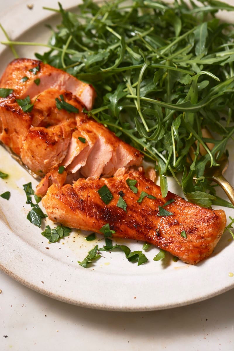 An air fryer trout fillet flaked apart on a plate with a salad. 