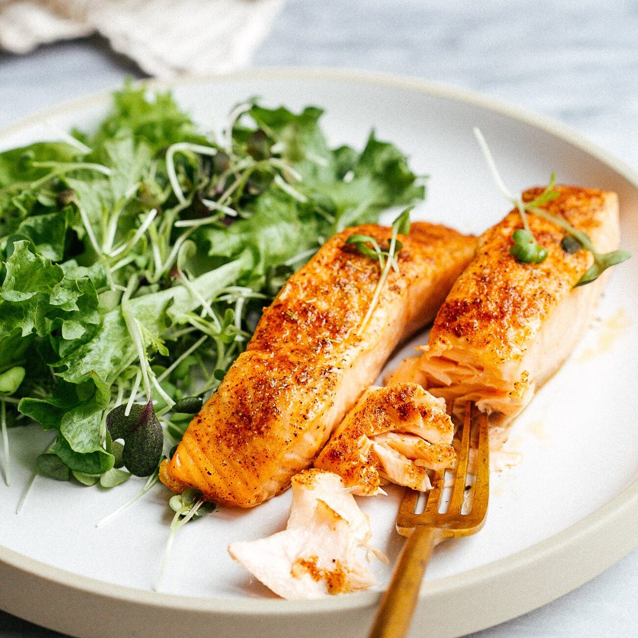 Closeup of a white plate with salmon and green salad.