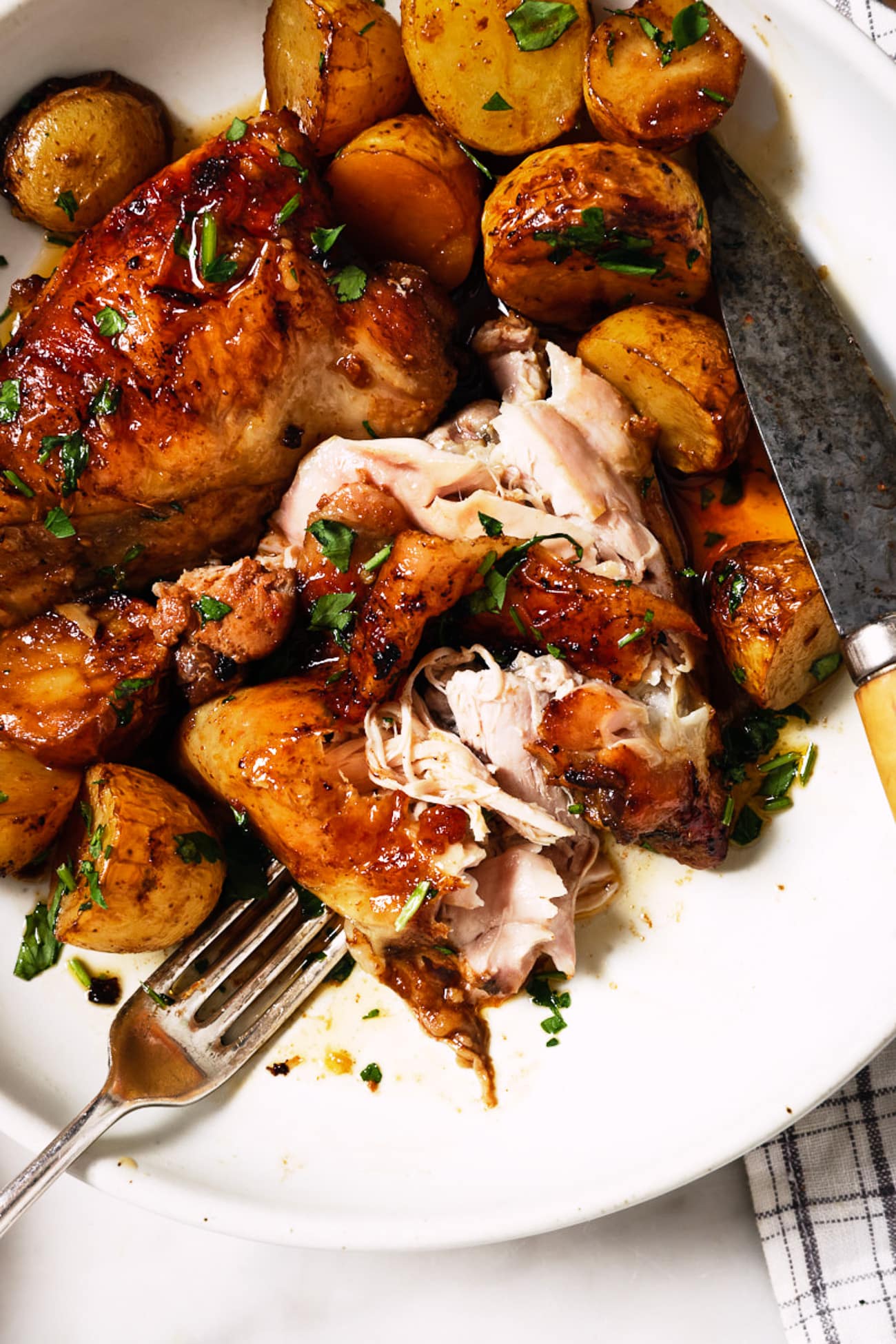 Chicken thighs with sweet potatoes on a white plate, with a fork and knife. 