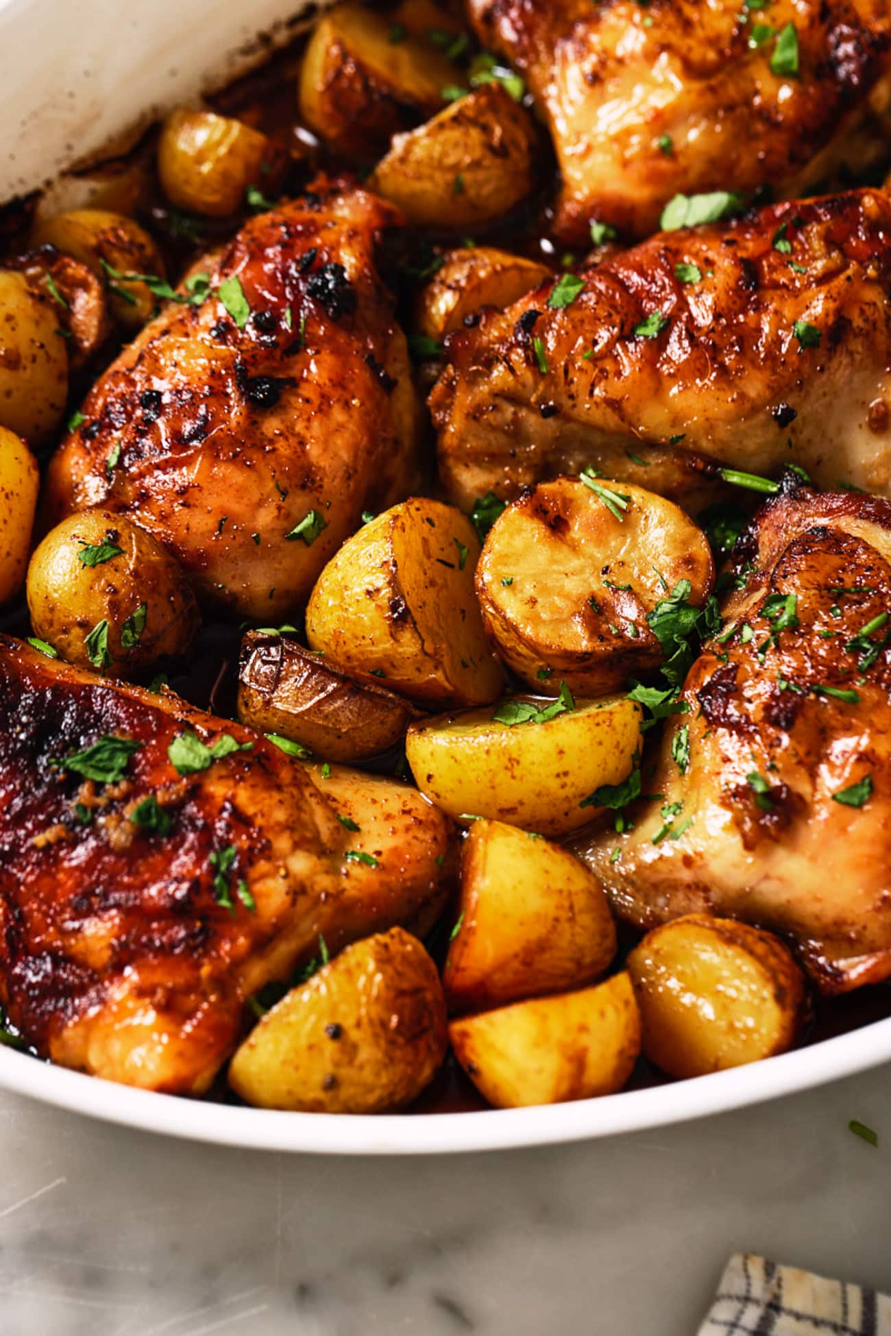 Chicken thighs with sweet potatoes in a white dish. 