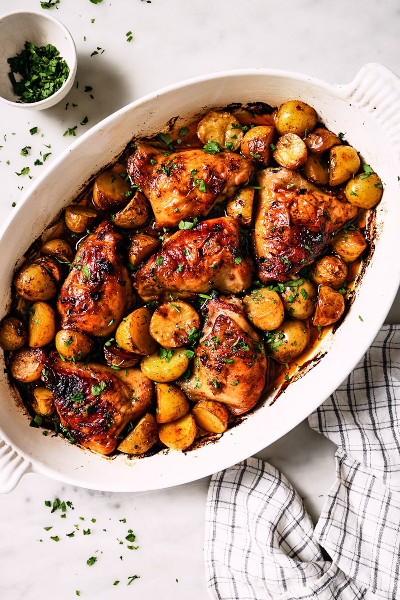 Chicken thighs with sweet potatoes on a white baking dish. 