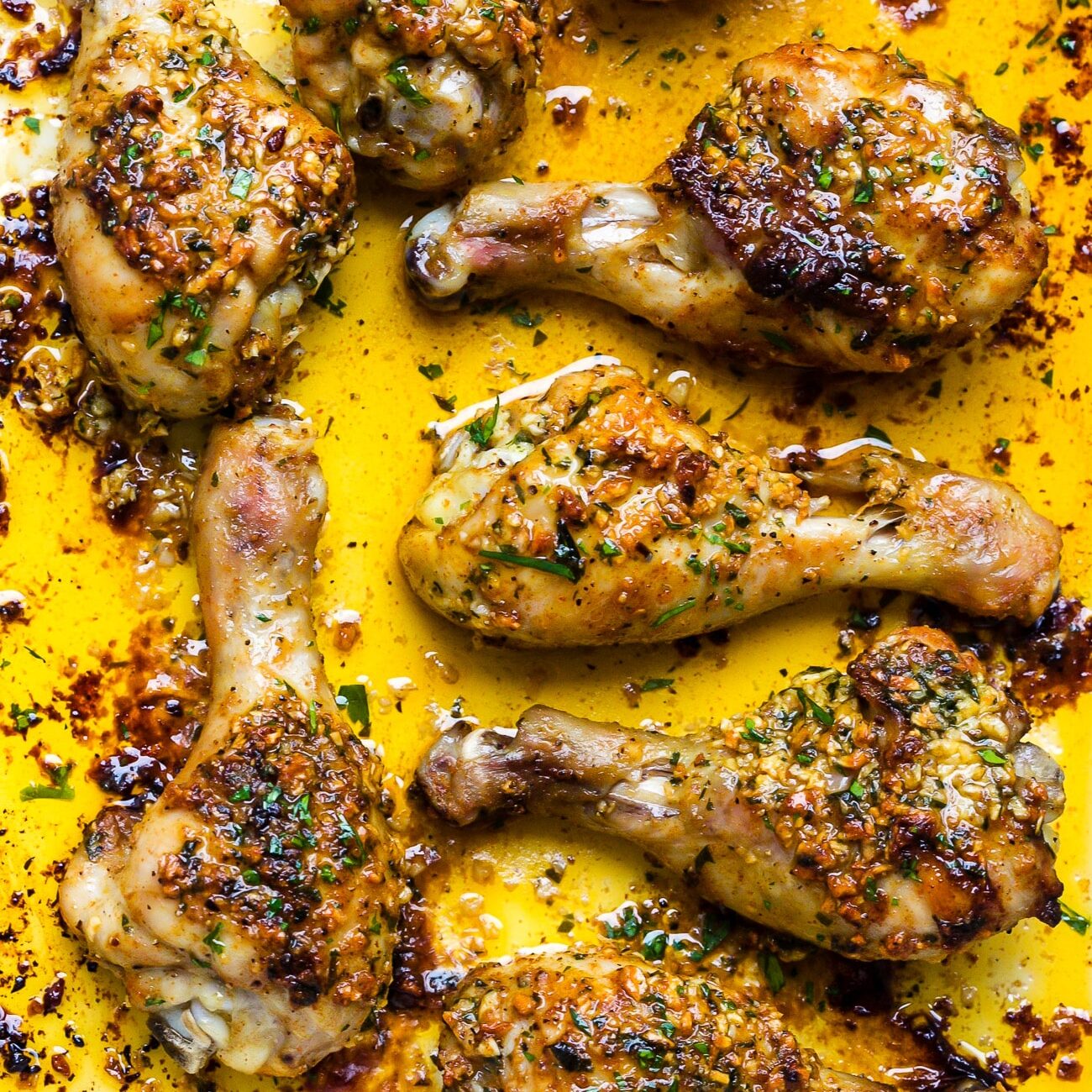 Close up of garlic butter baked chicken drumsticks in a white baking dish. One of my favorite date night dinner ideas.