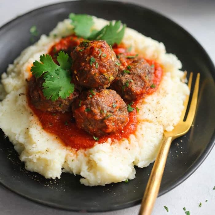 Turkey meatballs with mashed cauliflower on a black plate. One of my favorite date night dinner ideas.