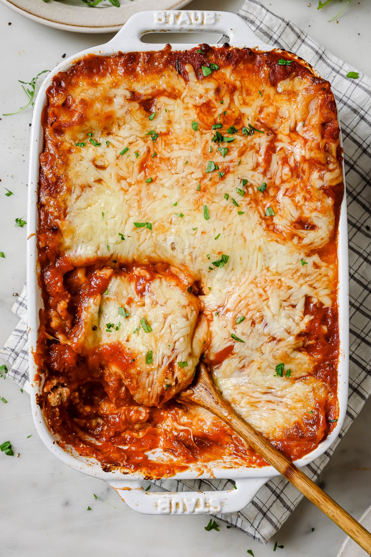 A casserole dish of lasagna rolls with a spoon dishing a serving out. 