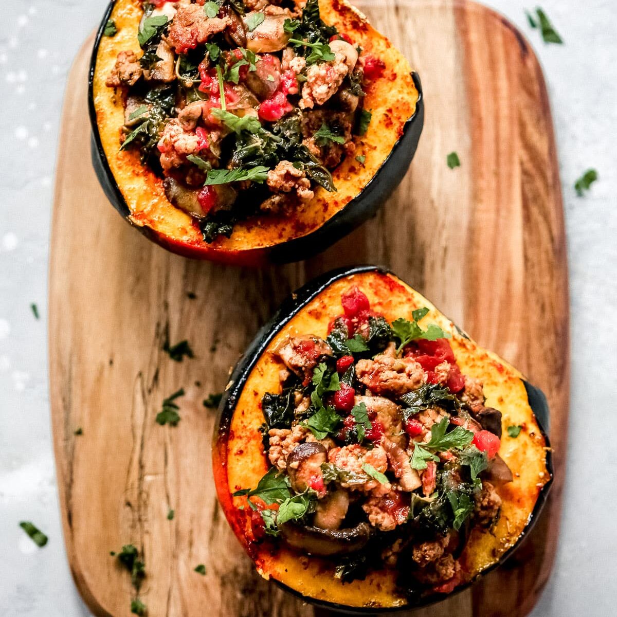 Sausage and kale stuffed acorn squash on a wooden cutting board. One of my favorite date night dinner ideas.