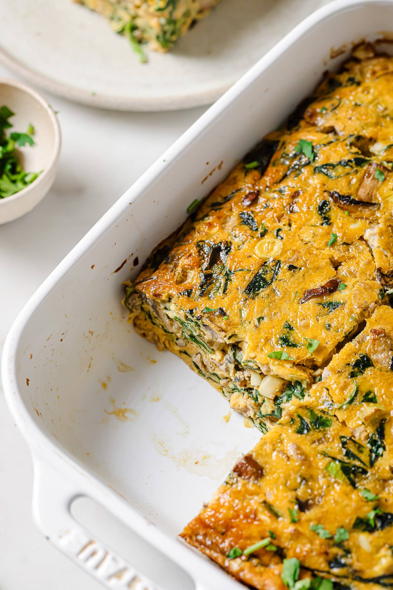 Spinach Mushroom Frittata in a white baking dish with one serving removed. 