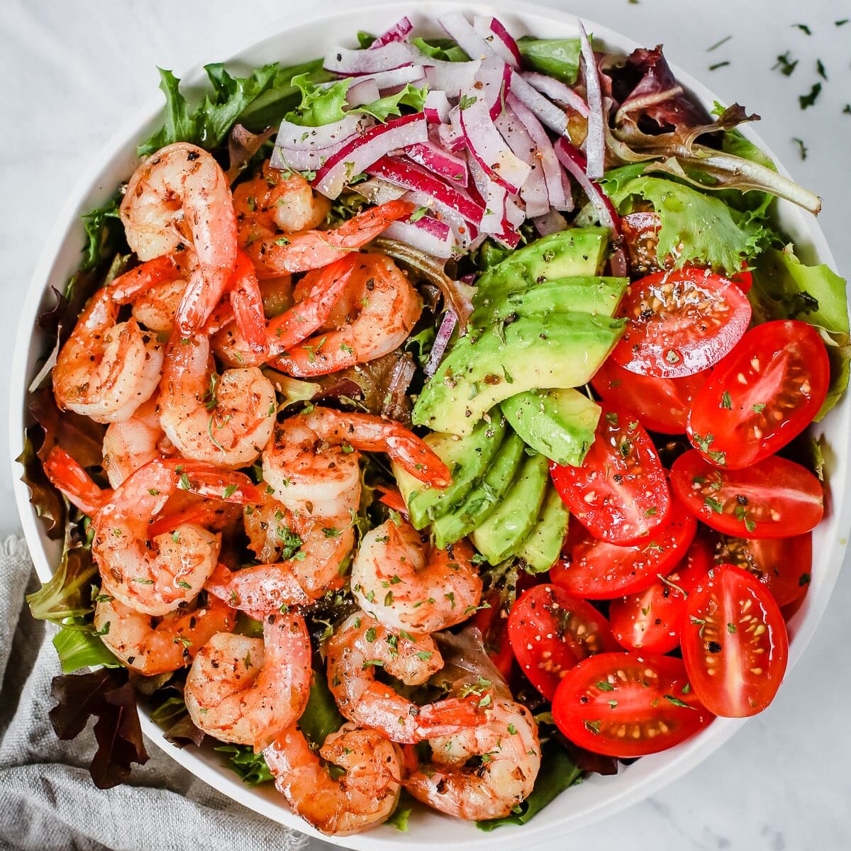 A bowl with shrimp, tomatoes, avocados, onions, and greens. One of my favorite date night dinner ideas.