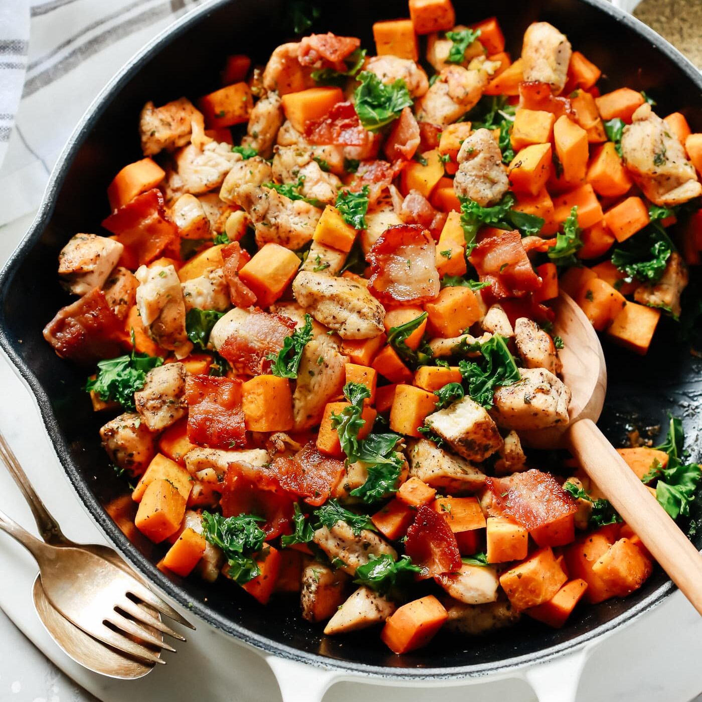 Overhead view of a white skillet containing kale, chicken and sweet potato. One of my favorite date night dinner ideas.