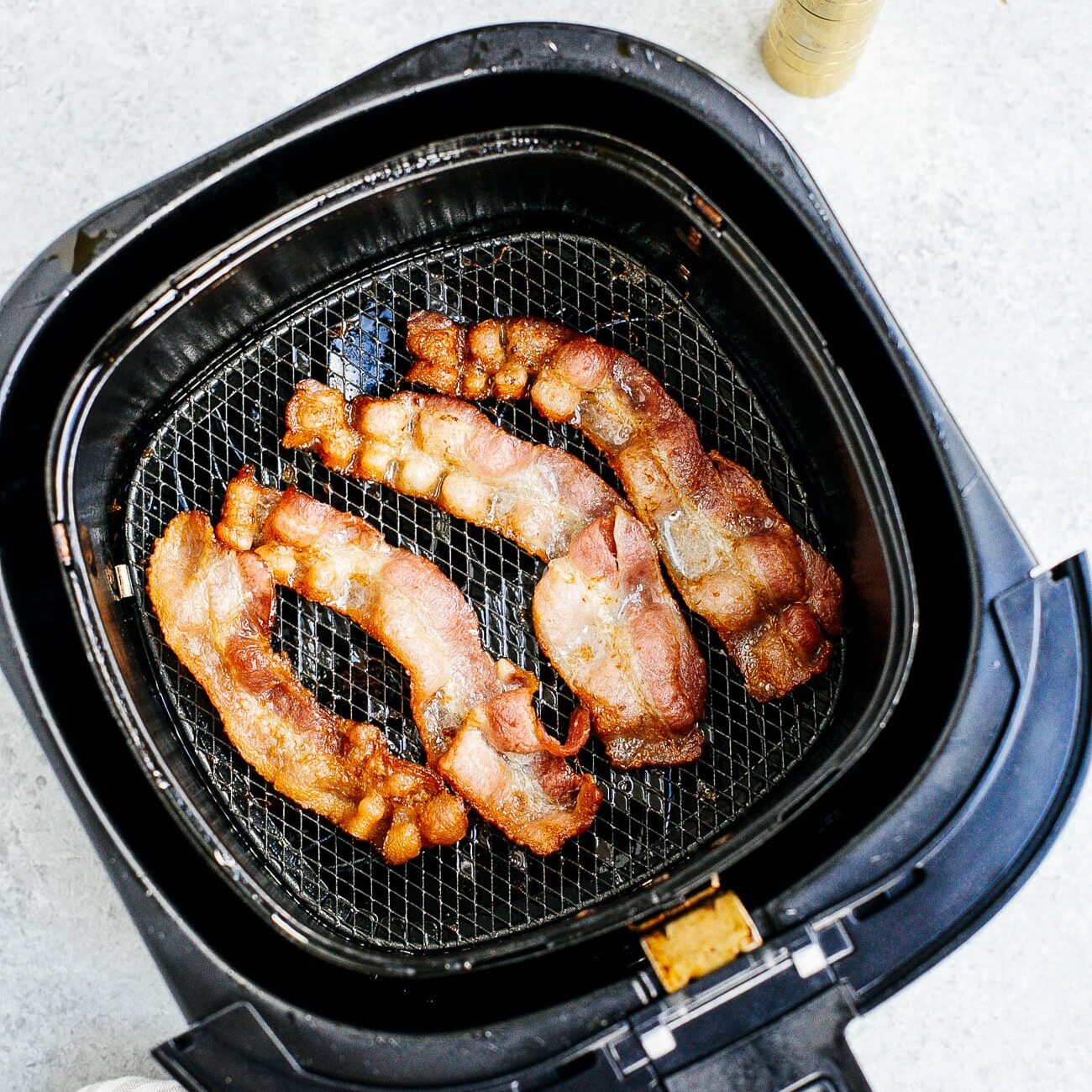 Overhead view of cooked bacon inside of a air fryer basket.