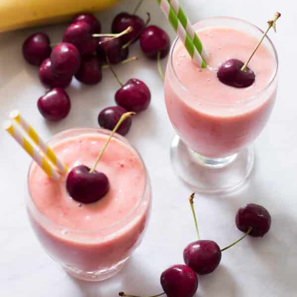 Cherry pineapple smoothies in glass cups with straws and a cherry on top.