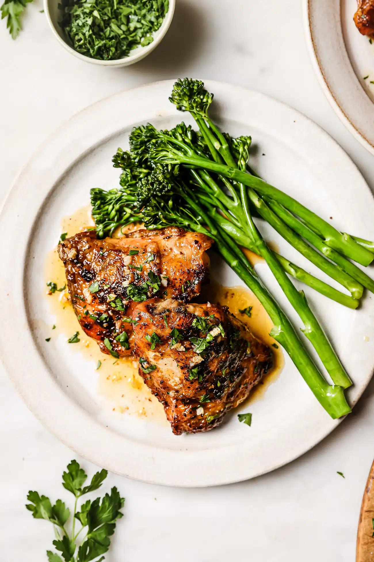 Chicken thighs on a white plate with green vegetables. 