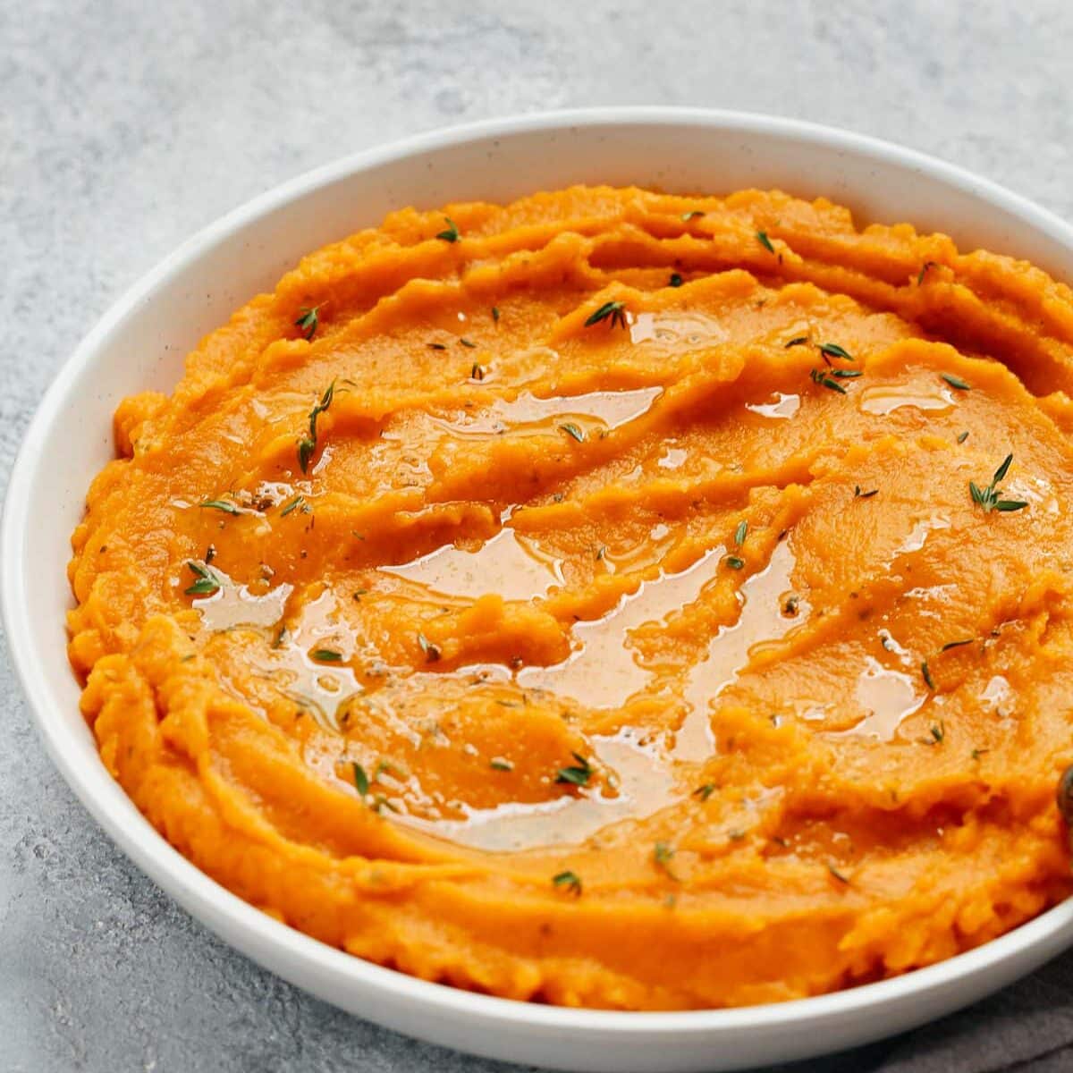 A close up of white bowl containing mashed sweet potato