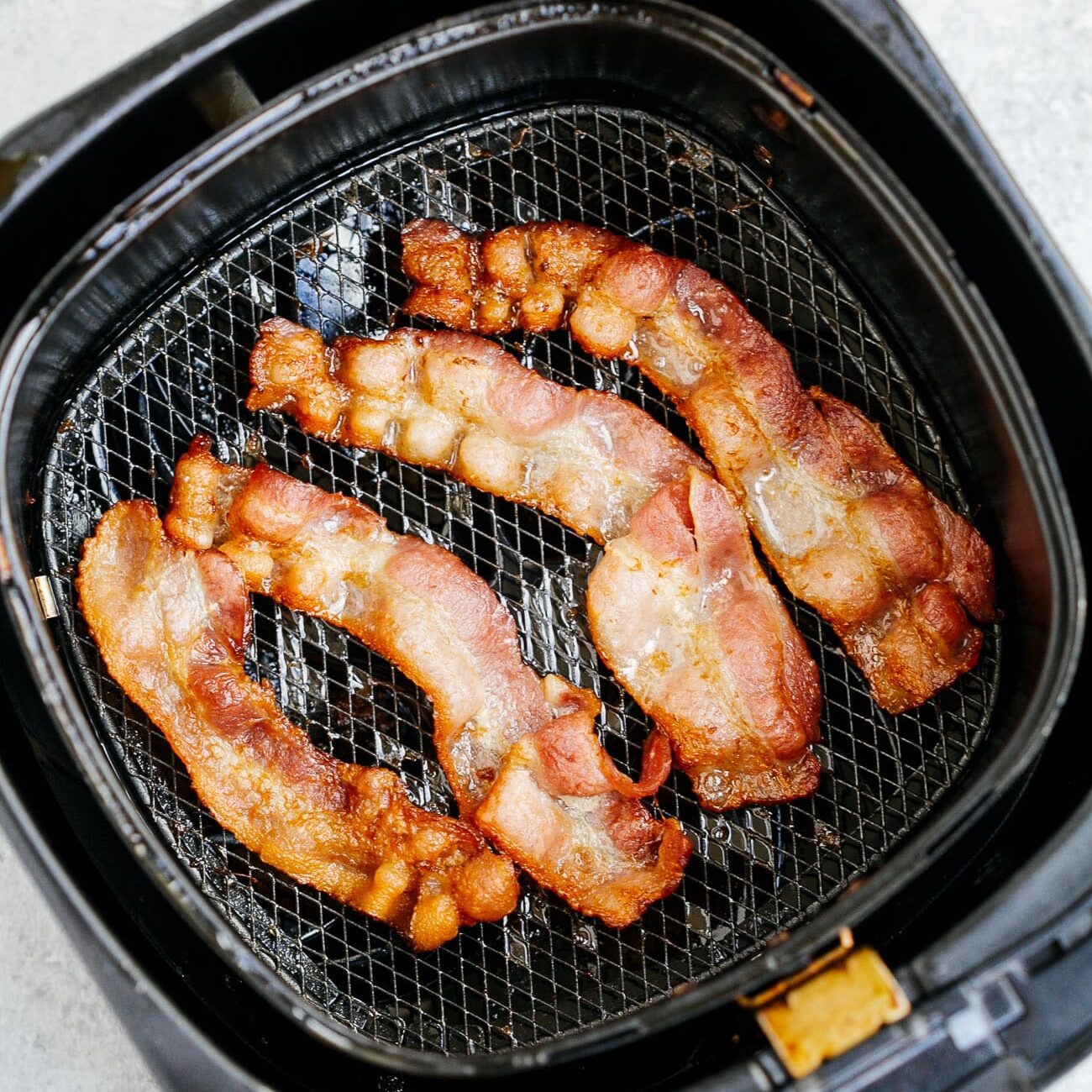 Overhead view of cooked bacon inside of an air fryer basket.
