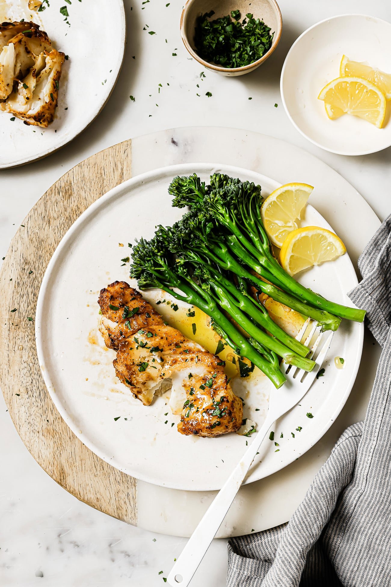 Air fryer cod on a white plate with green vegetables and lemon wedges.