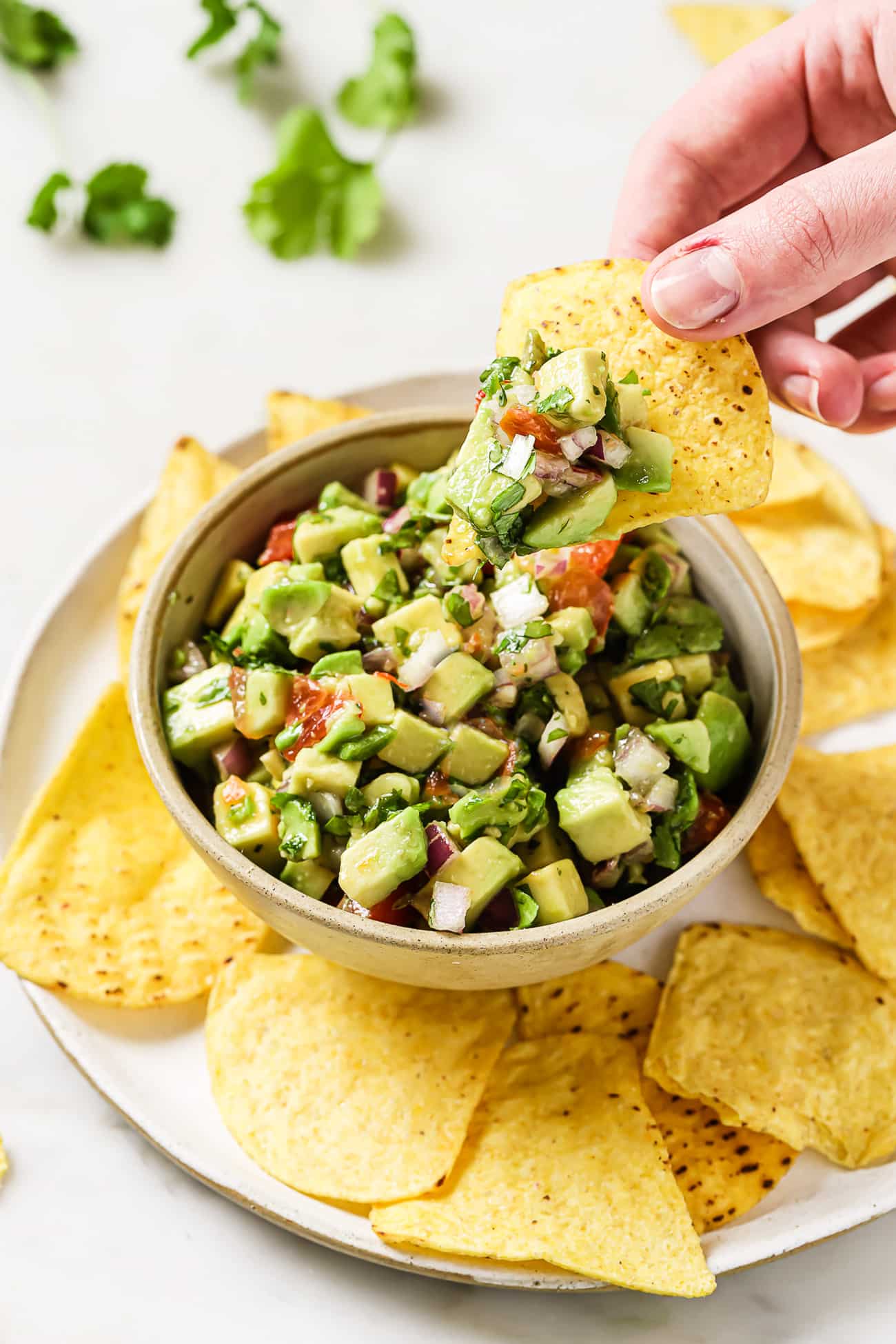 A bowl of avocado salsa on a plate of tortilla chips.