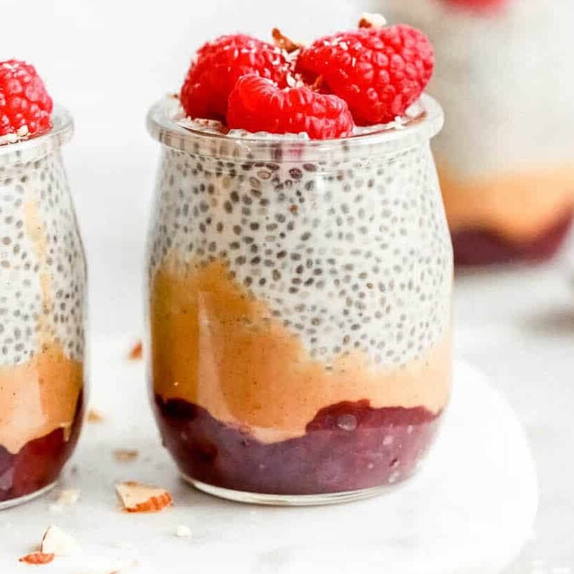 Chia seed pudding topped with raspberries in small glass jars.