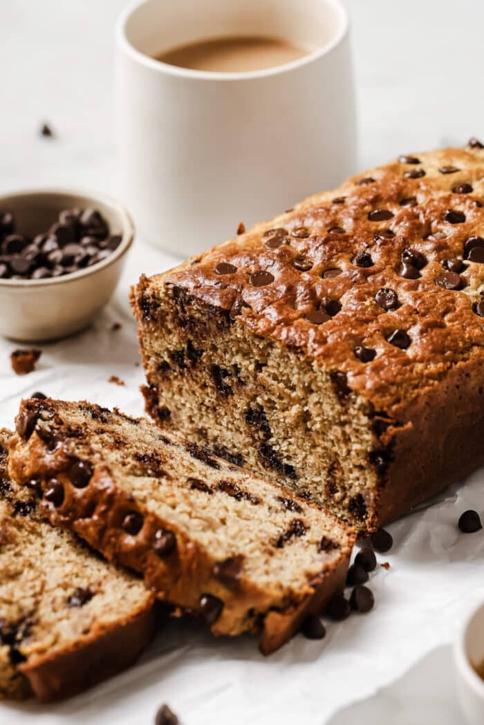 Gluten-free banana bread cut into slices with coffee and chocolate chips in the background.