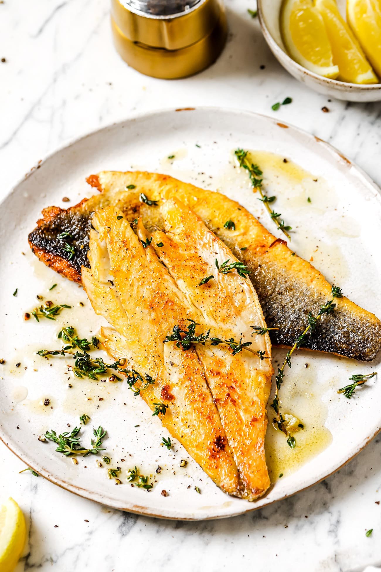 Garlic butter sea bass garnished with fresh thyme leaves on a white plate.