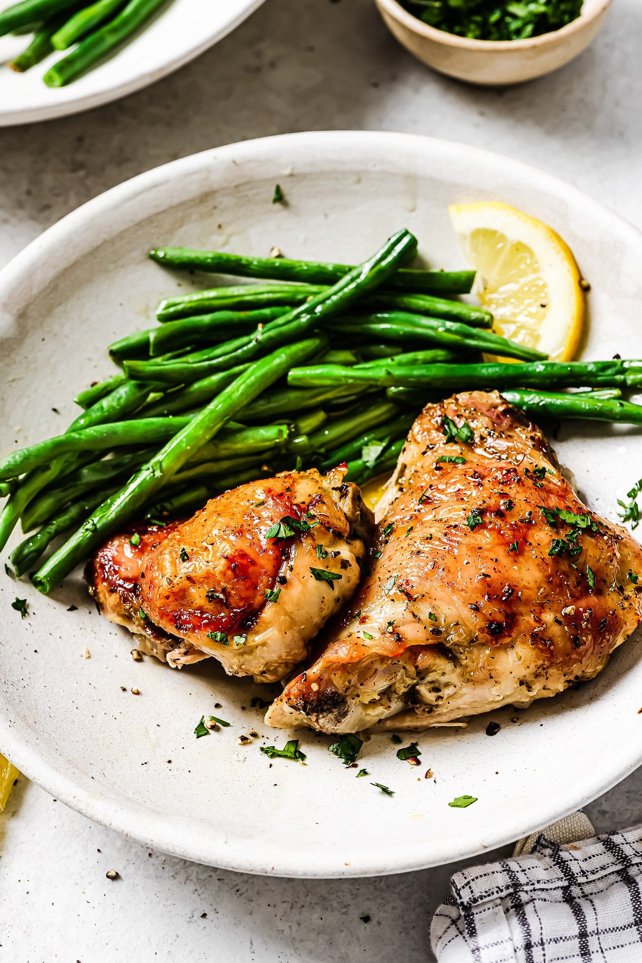 Lemon chicken thighs on a plate with green beans and a lemon wedge.