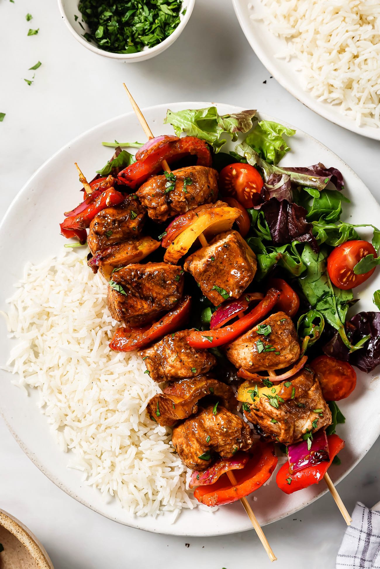 An overhead view of two chicken kabobs over a bed of rice and green salad.