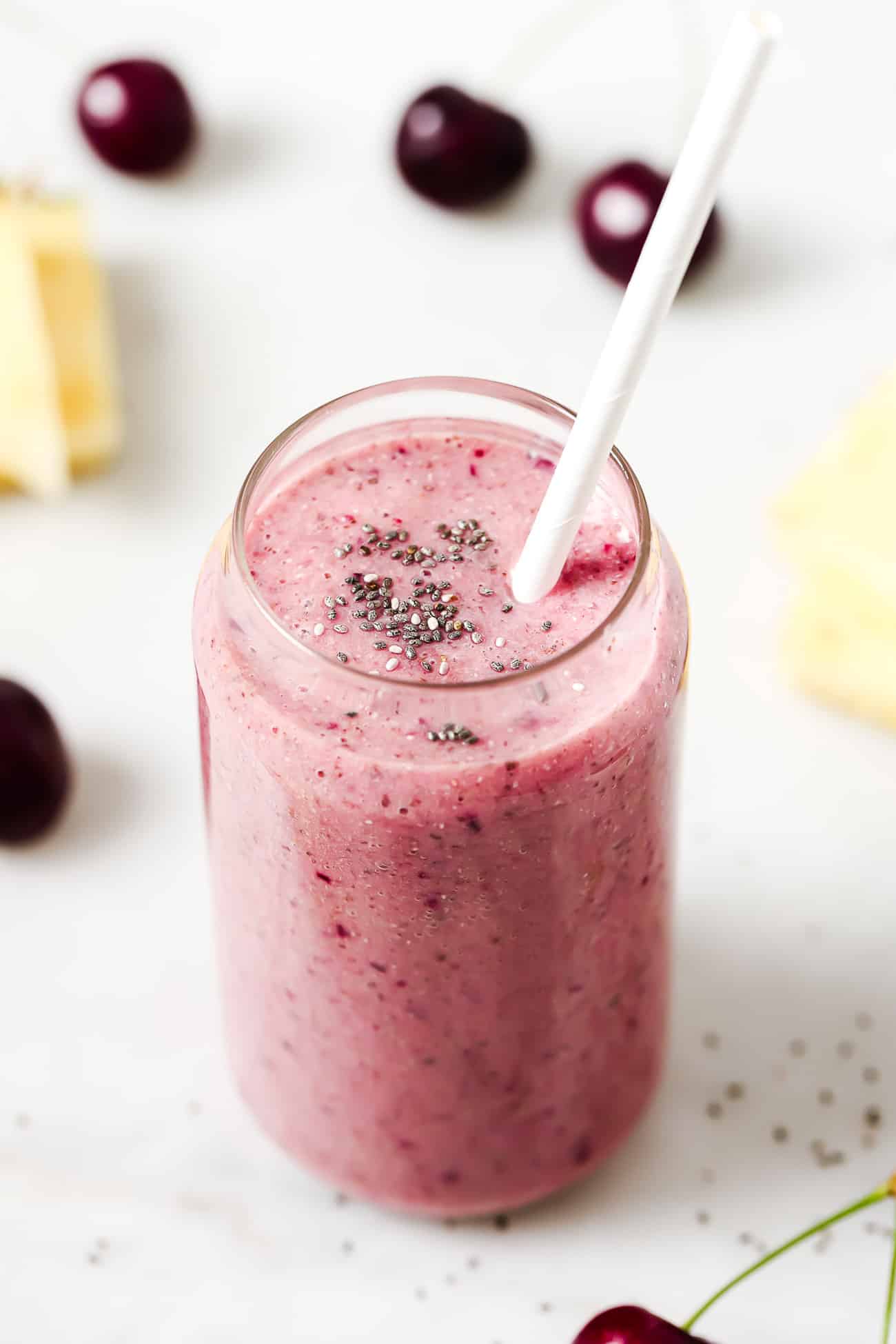 A cherry smoothie in a glass with chia seeds and a white straw.