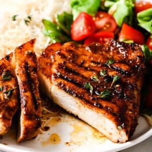 closeup of grilled pork chops on a plate with rice and salad