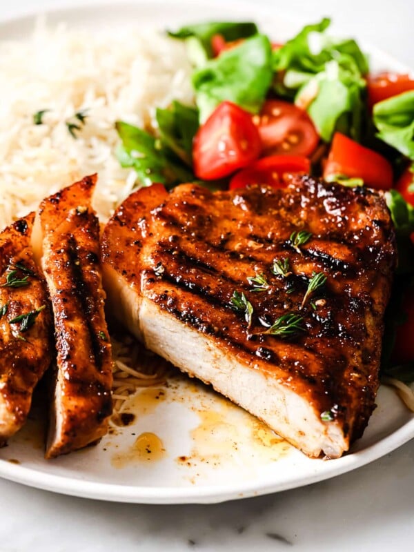 closeup of grilled pork chops on a plate with rice and salad