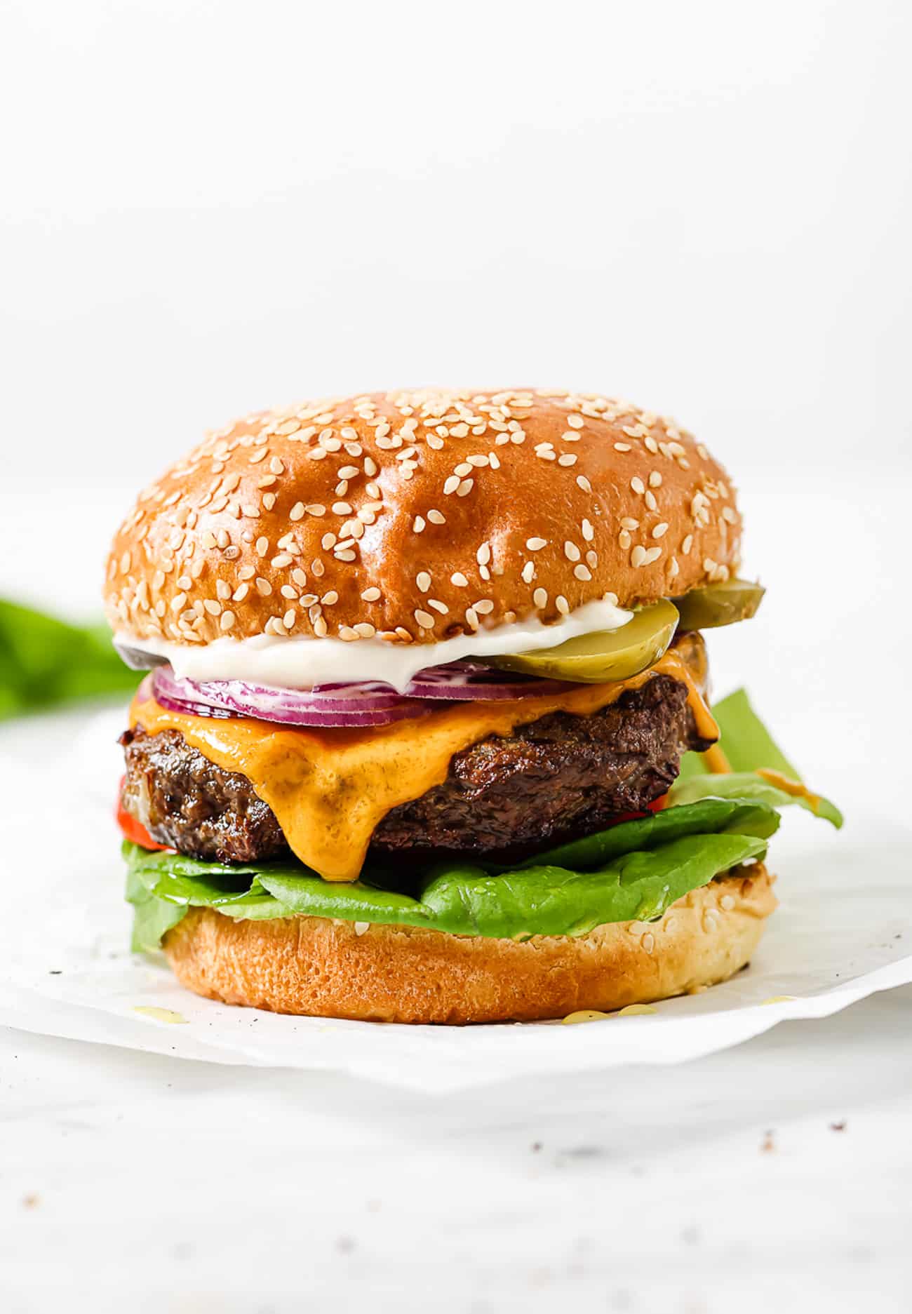 A side view of a hamburger with toppings on a sesame seed bun.