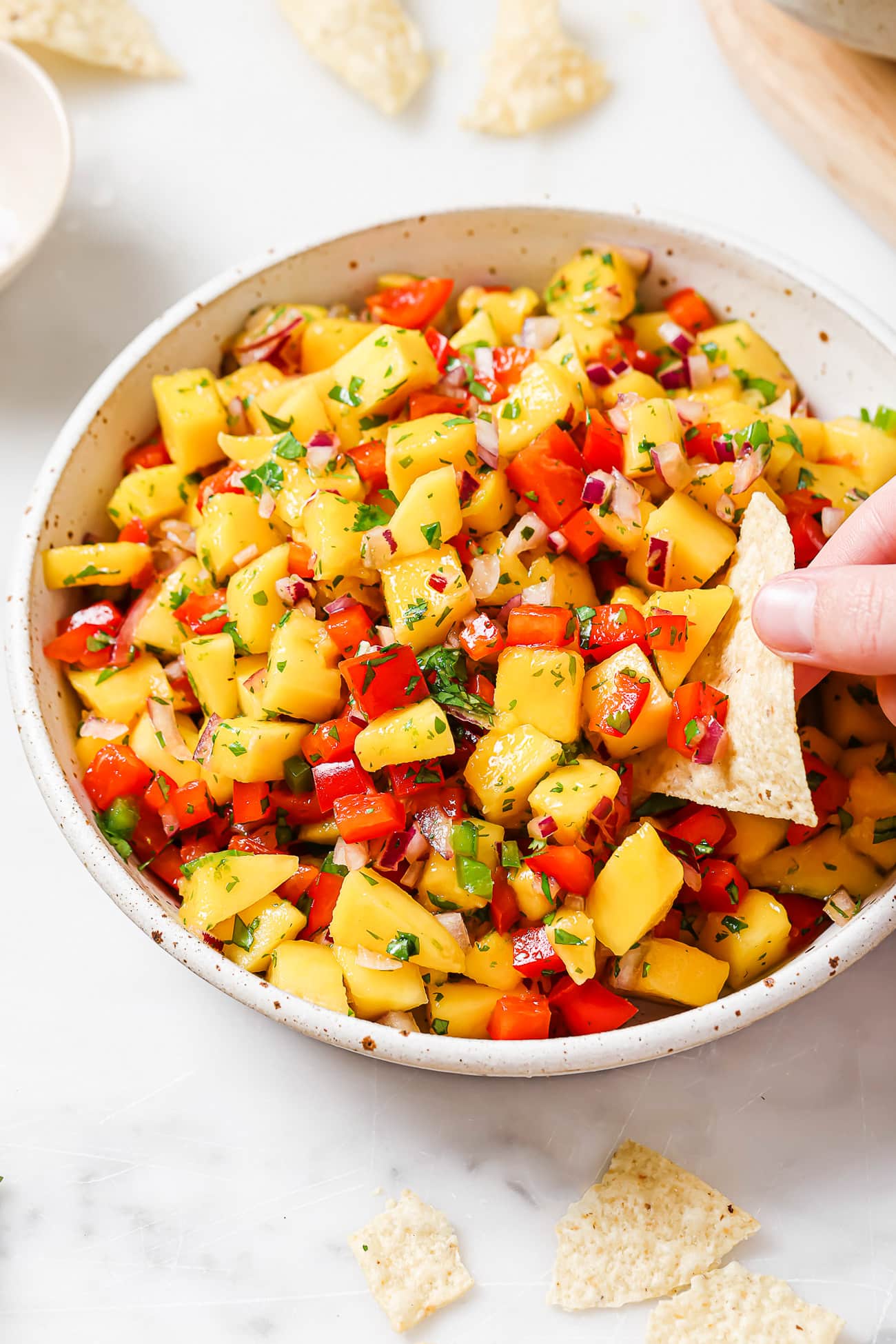 An overhead view of a chip scooping pineapple salsa out of a white bowl.