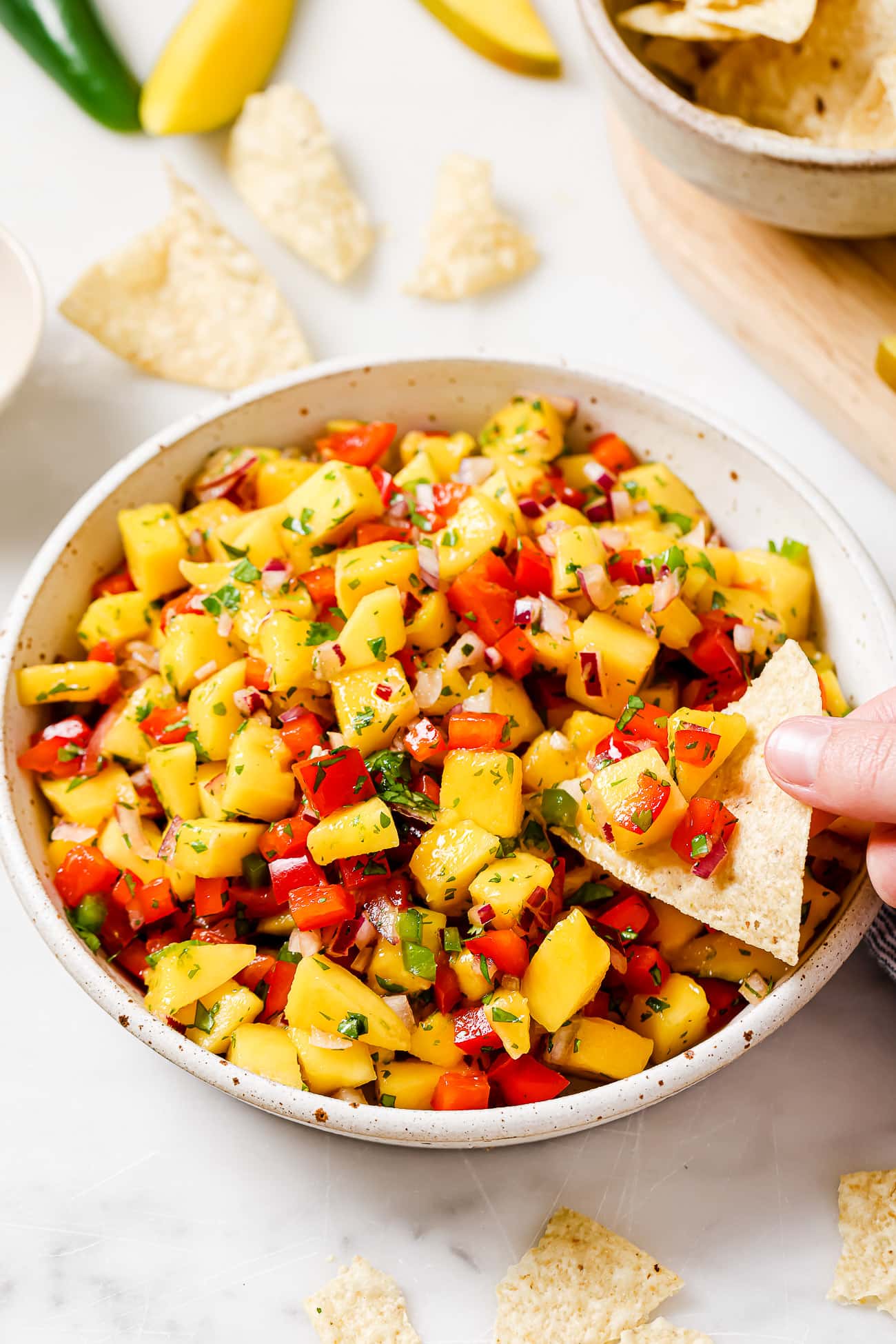 An overhead view of a tortilla chip scooping mango salsa from a large bowl.