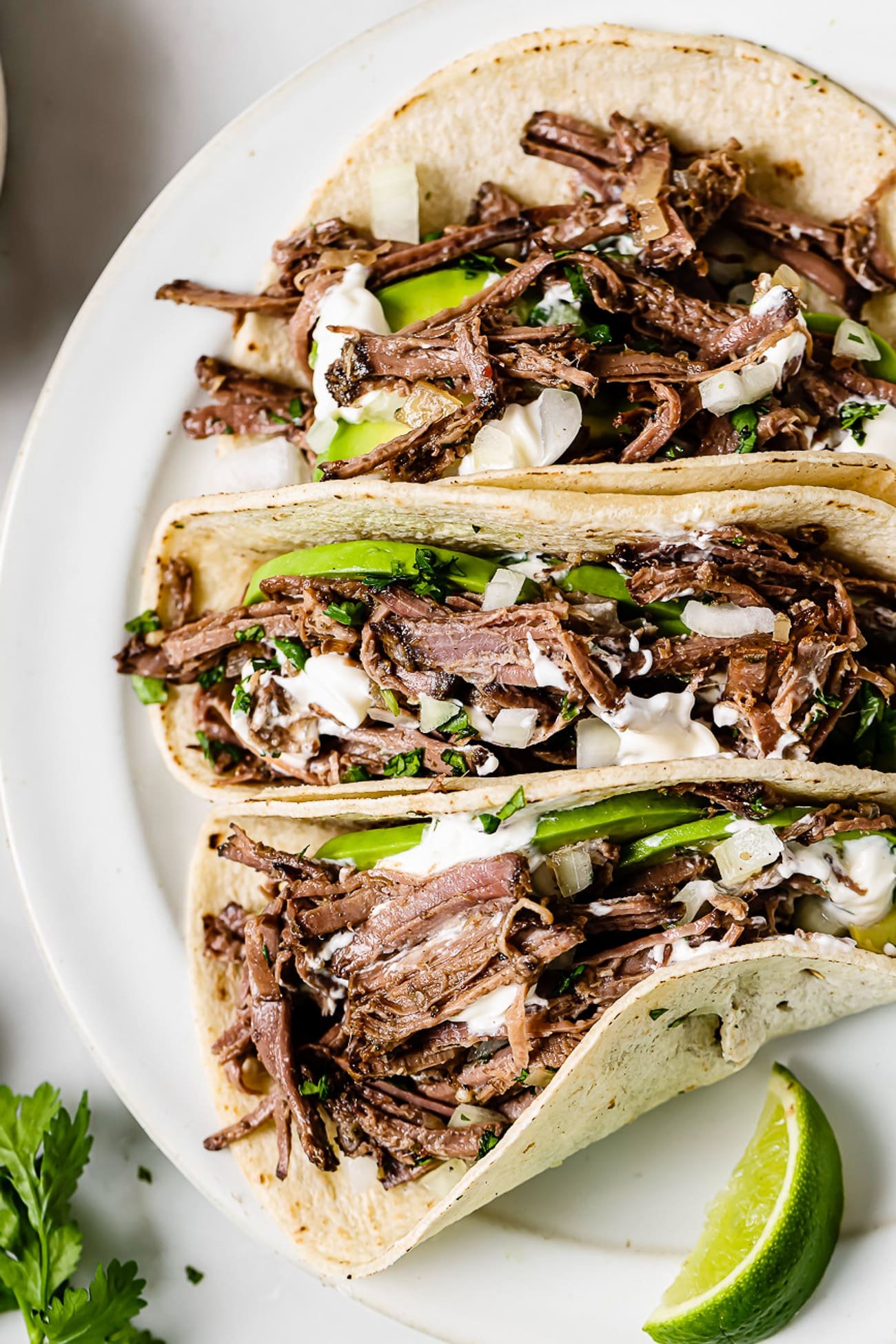 Barbacoa tacos topped with avocado, sour cream, cilantro, and onions.