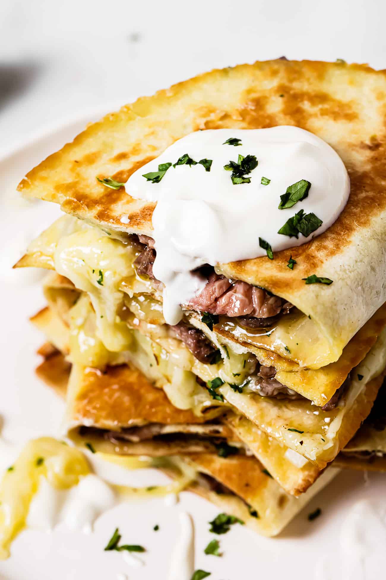 A stack of carne asada quesadillas topped with sour cream.