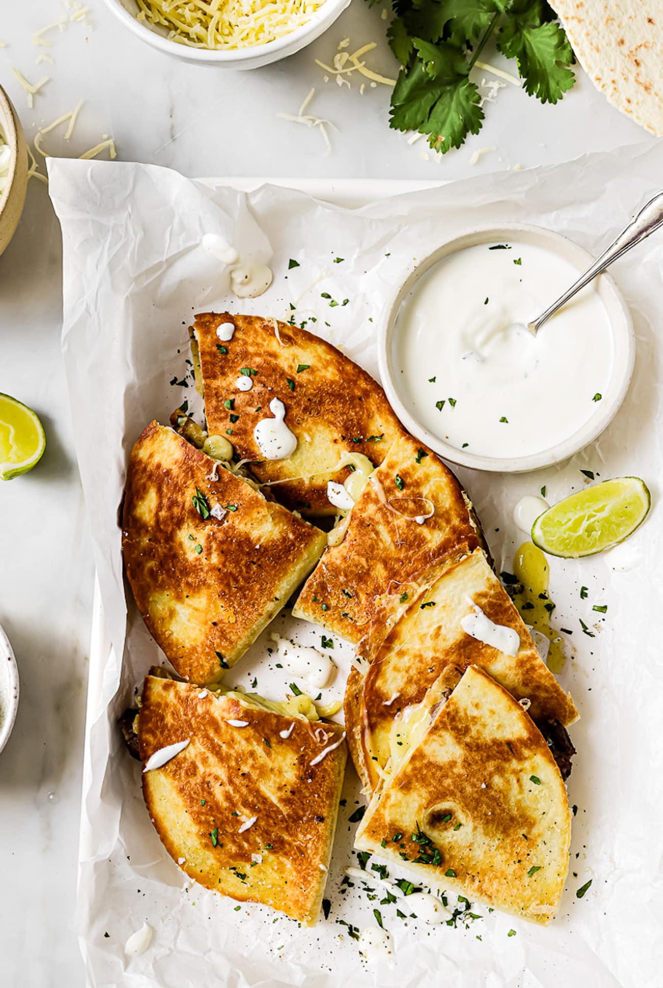 An overhead view of carne asada quesadillas on a serving platter with a side of sour cream.