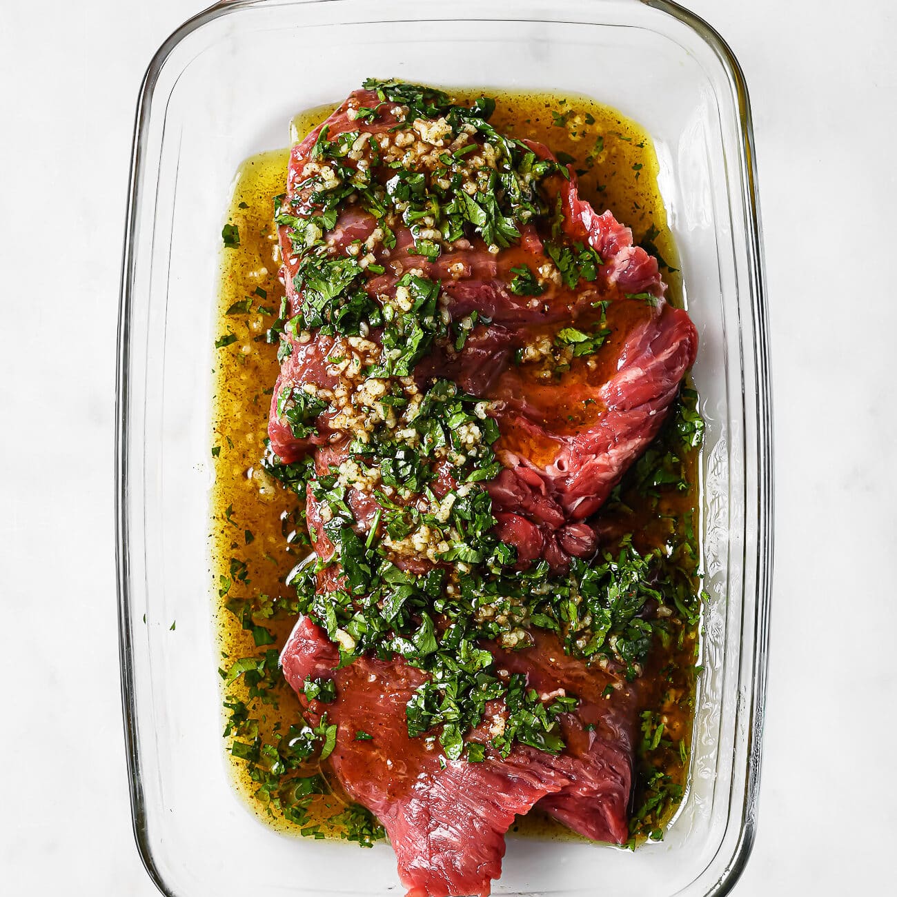 Marinated flank steak in a glass baking dish.